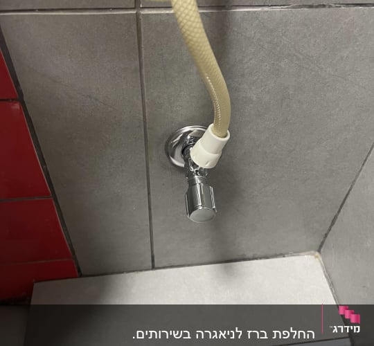צינור מחובר לברז על קיר אריחים אפור
